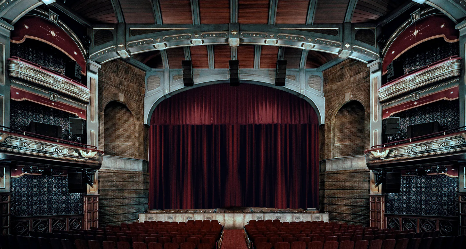 An ornate, empty theatre seen from the stalls, two figures standing before the red curtain